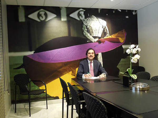 Ricardo Vilas de Escauriaza sentado a la mesa de la sala de reuniones, con un documento delante y un gran mural fotográfico de un torero al fondo
